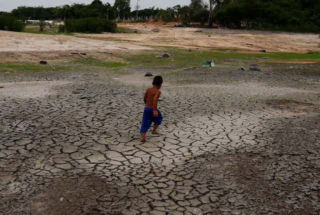 A boy walks on dry, crumbly ground that was once the bed of a great river