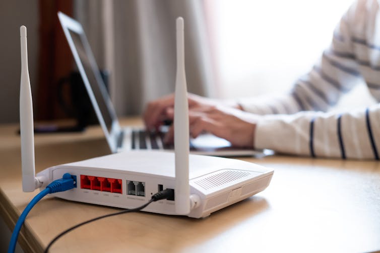 Photo of a white wifi router on a desk with a person working on laptop in the backround