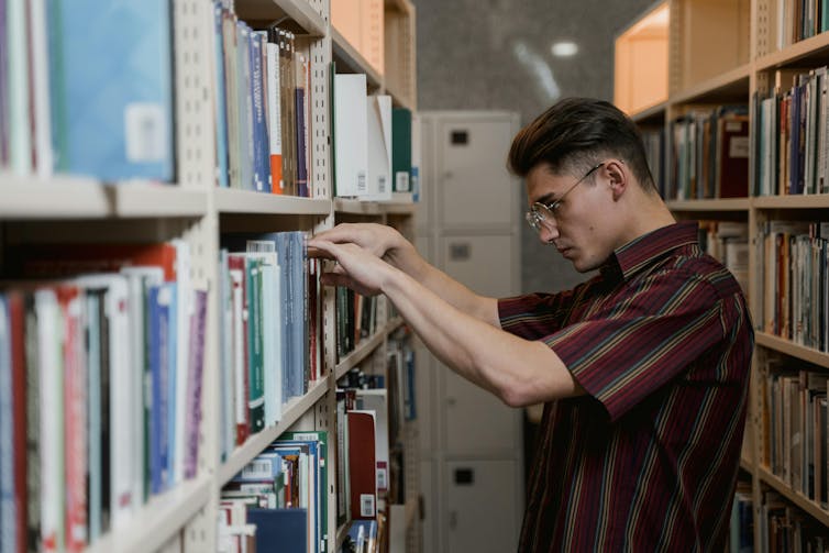 A young man searches the shelves of a library.