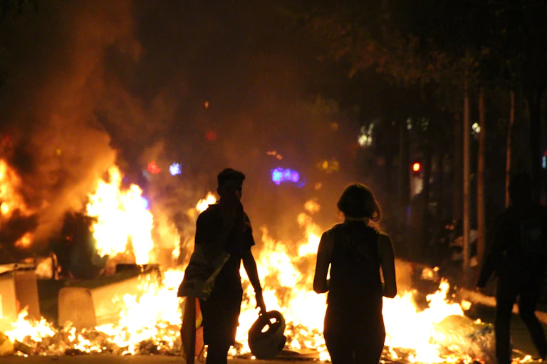 two silhouettes are seen backlit by the flames of a bonfire