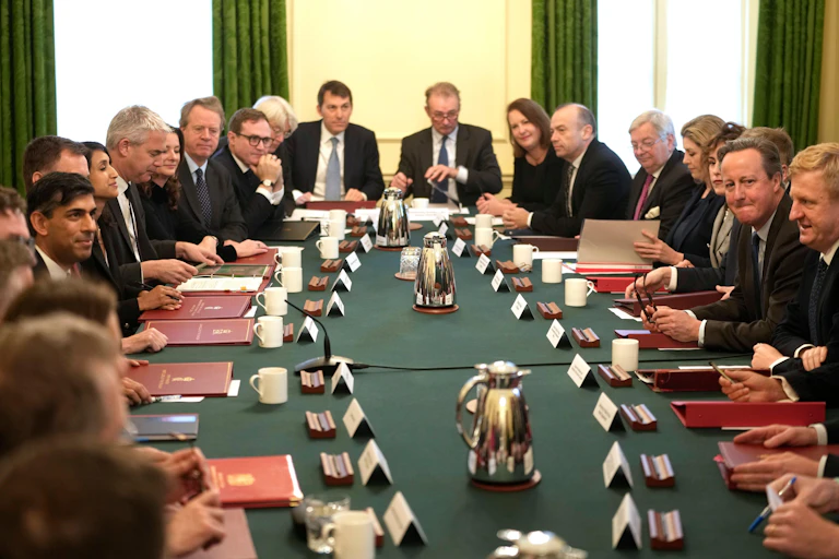 Cabinet ministers seated around a long table, each with a red folder and name placard in front of them. Rishi Sunak and David Cameron are seated opposite each other.