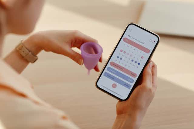 Gros plan sur une femme faisant le suivi de son cycle menstruel à l'aide d'un calendrier auquel elle accède via une application sur son smartphone.