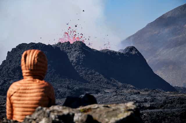 A person looks on at lava erupting from a caldera.