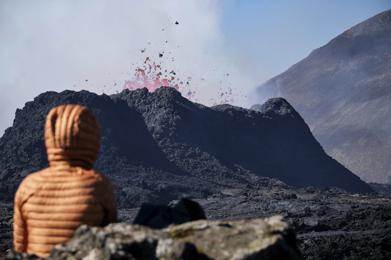 A person looks on at lava erupting from a caldera.