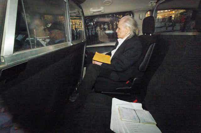 interior shot of an older man sitting in the back of a police car