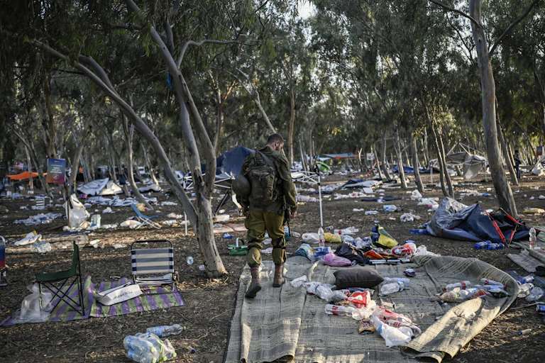 Un homme en treillis dans un sous-bois parmi des restes éparpillés d'un campement