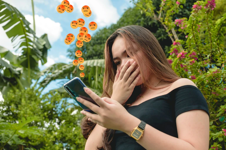 jeune femme regarde son téléphones, émojis de colère