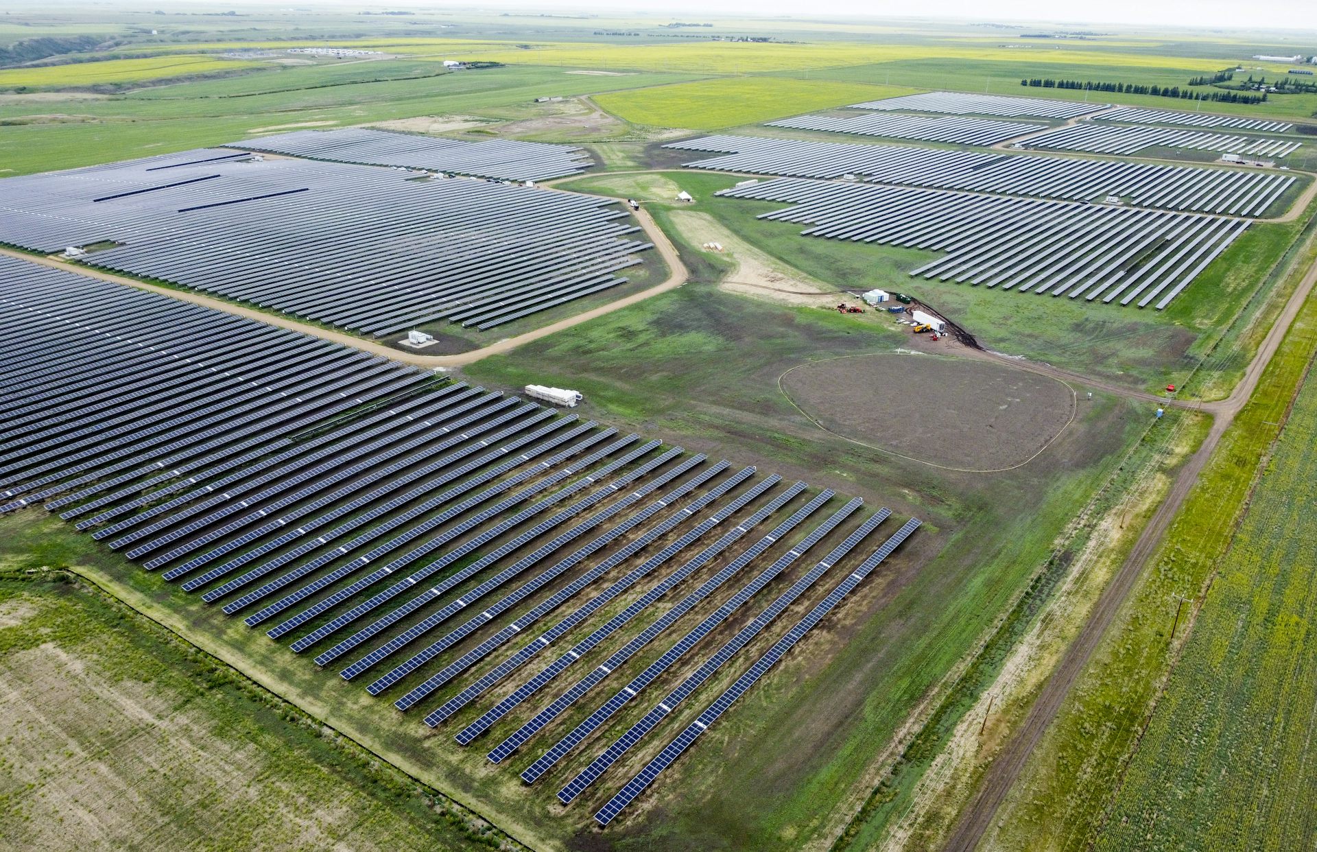 A field of solar panels and scattered buildings seen under a cloudy sky.