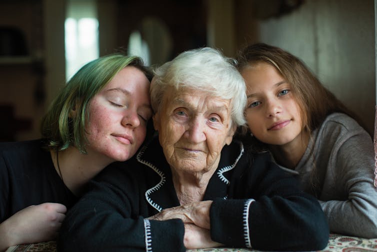 An elderly lady sits between two young women.
