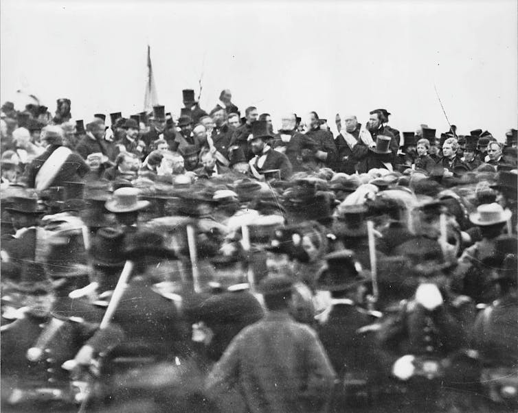 A black and white photo of a crowd of men in coats and stovepipe hats.