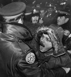 A black-and-white photo of police officer holding back a protester