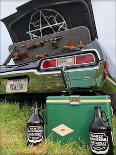 Trunk of car opened with weapons displayed, with two jugs of beer and a cooler in the foreground.