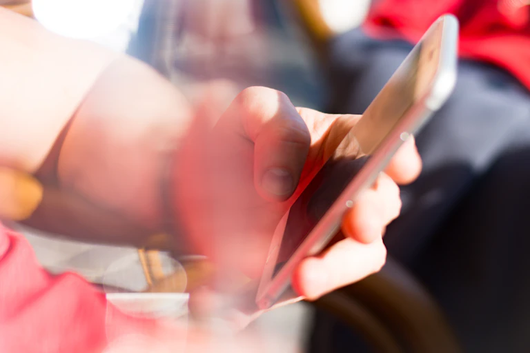 A hand holding a smartphone in a busy outdoor setting