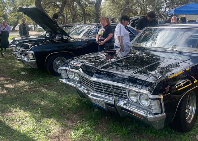 Fans inspect two black vintage cars.