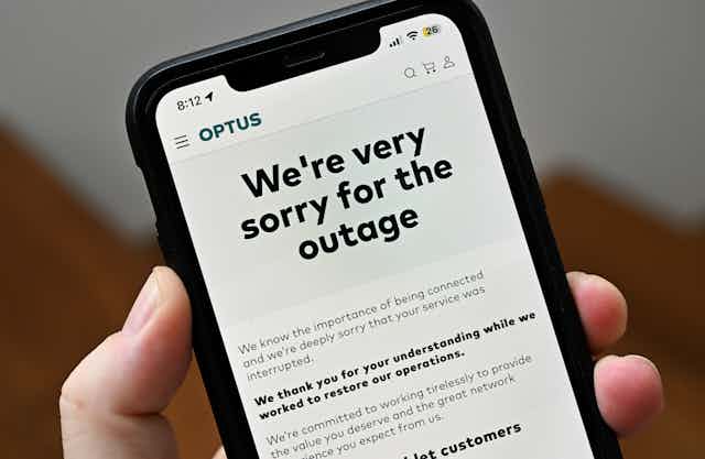 Unidentified hand holding a phone showing a note from Optus apologising for the outage