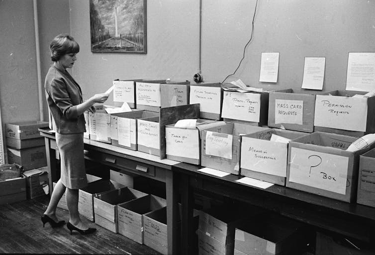 A woman in the 1960s standing in front of a table filled with boxes to categorise letters