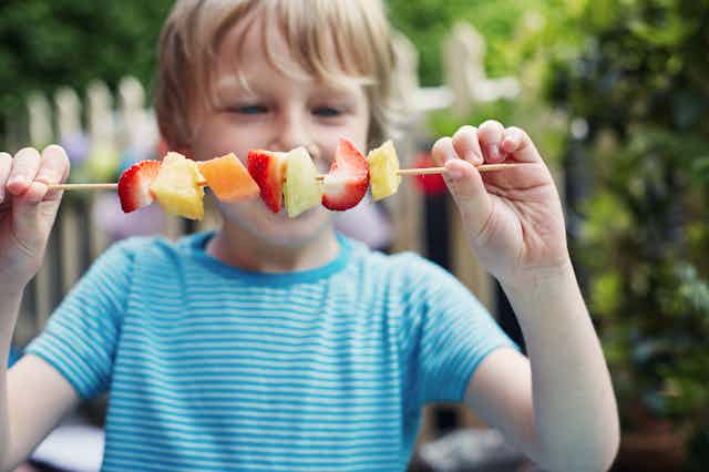 A child holds a fruit skewer.
