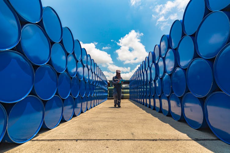 hombre junto a barriles de petróleo apilados