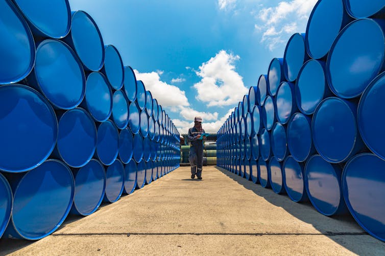 A worker stands near stacked oil barrels.