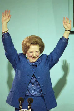 Woman in blue suit raises arms smiling