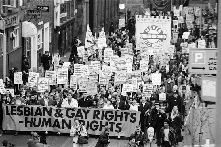 Black and white photo of protest march with placards and banner reading "Lesbian and gay rights - human rights"