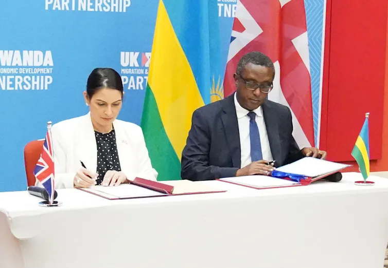 Priti Patel and Rwandan minister Vincent Biruta sit side by side at a table, signing the deal.