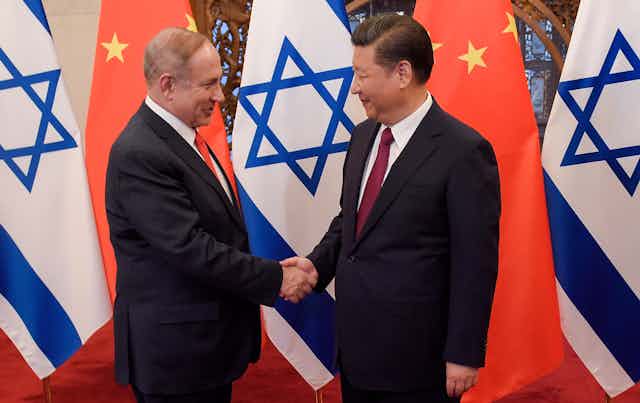 Israeli president Benjamin Netanyahu shakes hands wioth Chinese president Xi Jinping with the two ocuntries' flags in the background.
