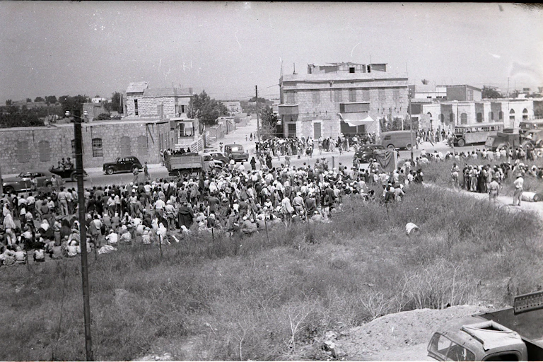 Fotografía de camiones llenos de gente que circulan por una calle, con una pista llena de gente pendiente de qué ocurre.