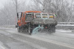Salt is sprayed from the back of a truck on a snowy road.