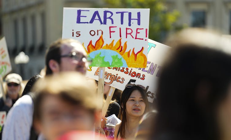 Someone carries a sign that reads Earth is on Fire at a protest.