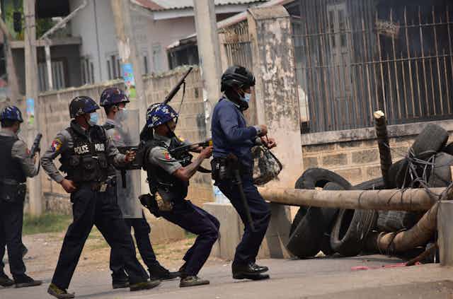 Myanmar military personnel firing across a barricade on a city street.