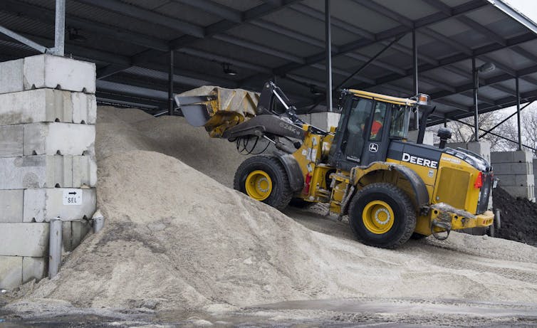 A heavy digger drives up a mound of salt.