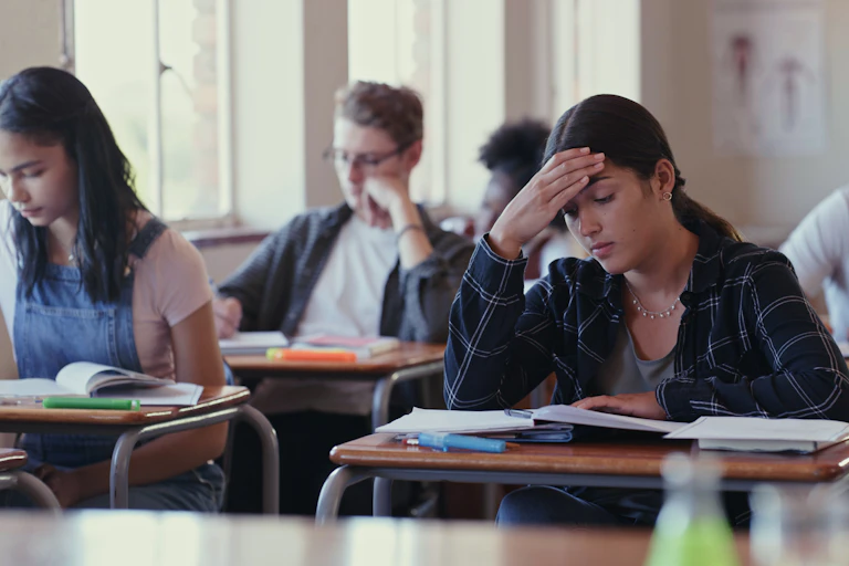 Students sit at desks with books open in front of them.