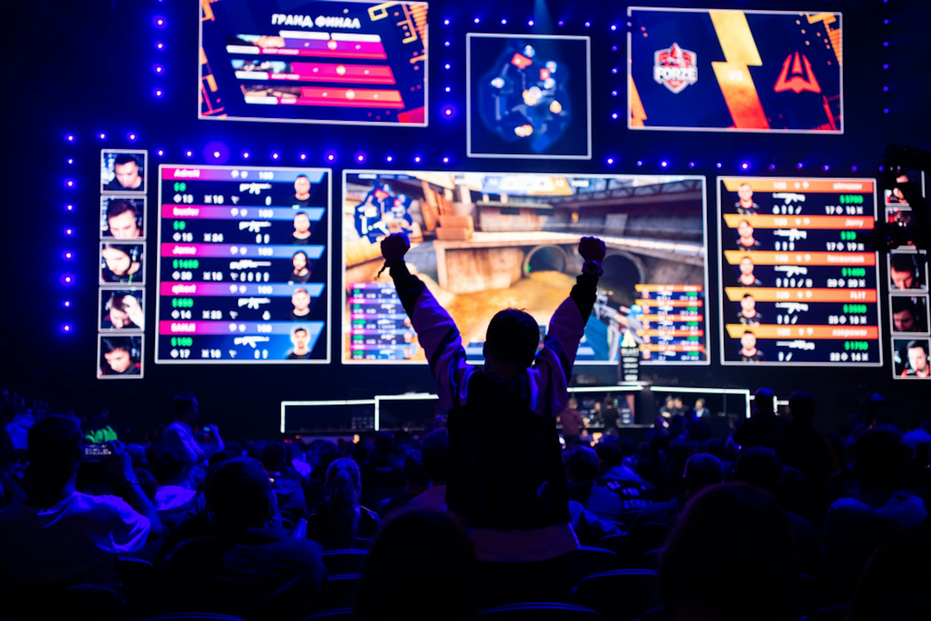  esports gaming event. Big illuminated main stage and screen and a fan with a hands raised at arena.