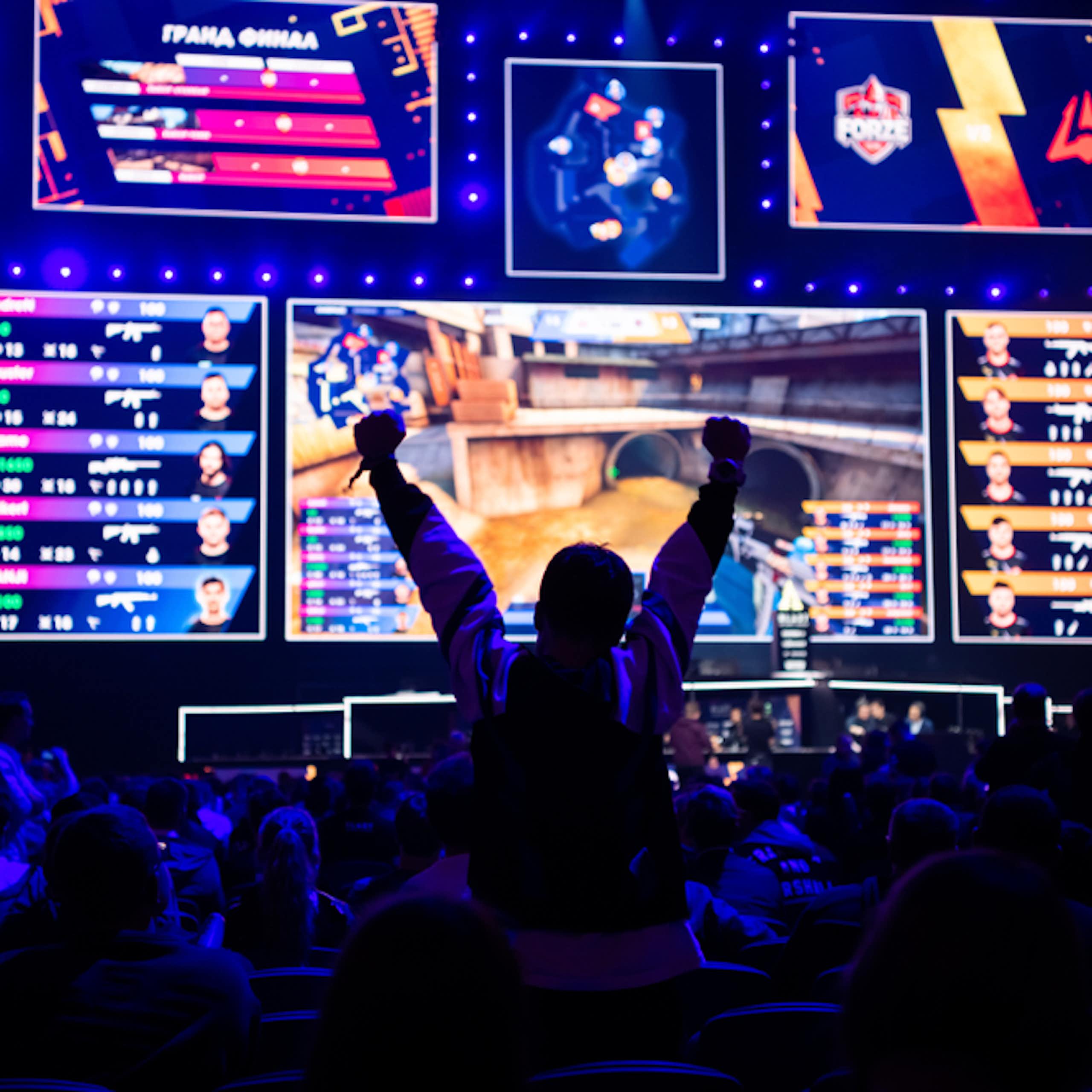  esports gaming event. Big illuminated main stage and screen and a fan with a hands raised at arena.