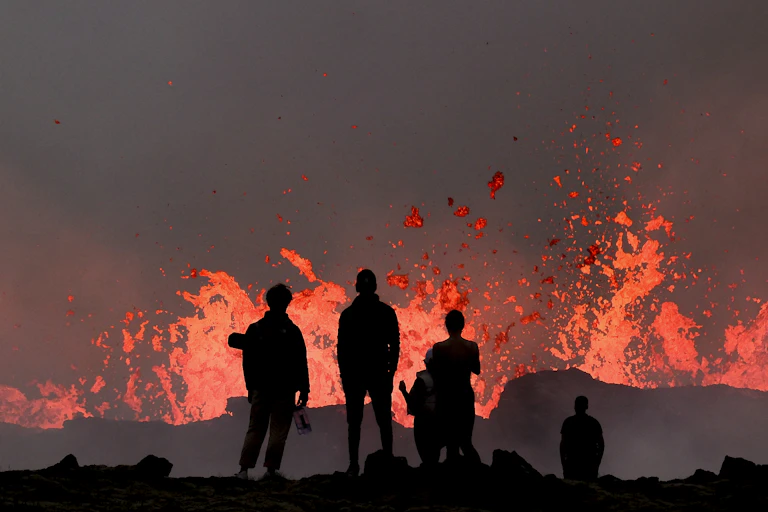 Several people watch a volcano's low-level eruption. The people are silhouetted against the lava.