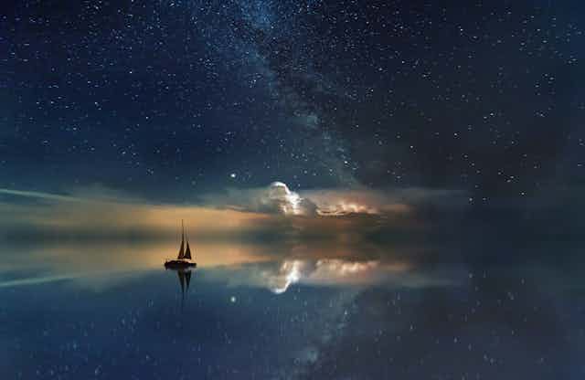 Un bateau glissant sur une mer d’huile dans laquelle se reflète le ciel étoilé