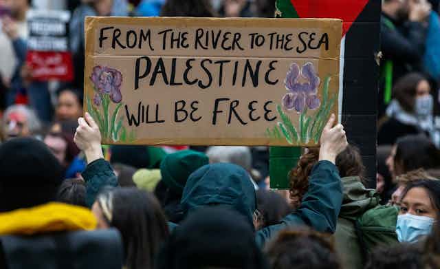 A protester holds up a sign reading 'From the River to the Sea Palestine will be free.'