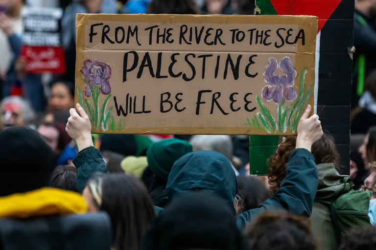 A protester holds up a sign reading 'From the River to the Sea Palestine will be free.'