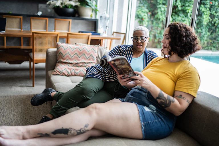 Two people sit on a couch, quoting from a book