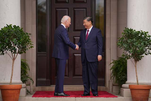 Joe Biden and Xi Jinping shake hands in front of a door
