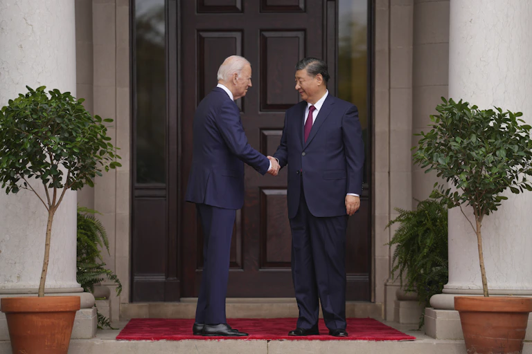 Joe Biden and Xi Jinping shake hands in front of a door