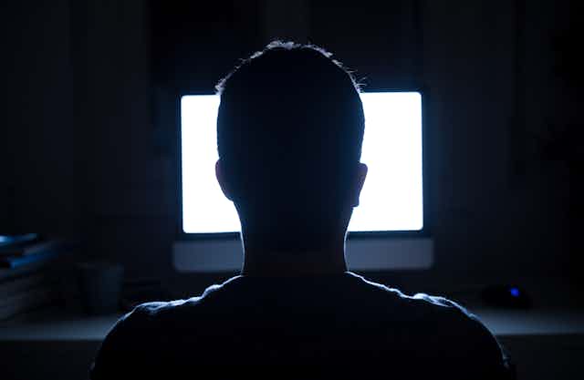 A person sits in front of a bright screen in a dark room. 