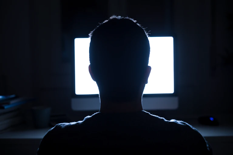 A person sits in front of a bright screen in a dark room.