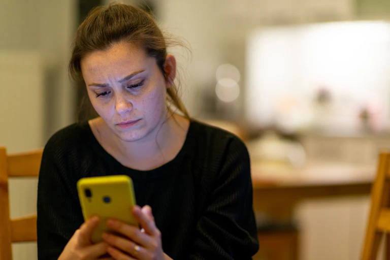 A woman looks worriedly at her phone.