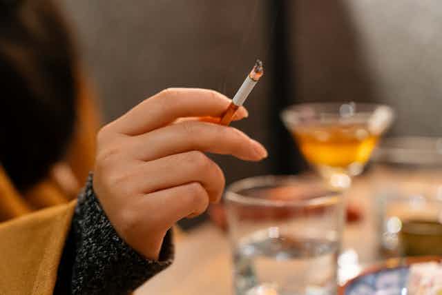 Woman holding cigarette, glasses of alcoholic drinks in background