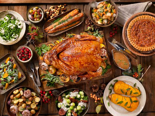 A large Thanksgiving dinner with a roasted turkey in the middle surrounded by vegetables, salad, cranberries and pie.