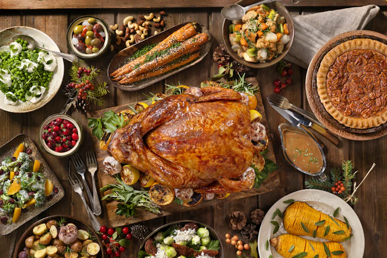 A large Thanksgiving dinner with a roasted turkey in the middle surrounded by vegetables, salad, cranberries and pie.
