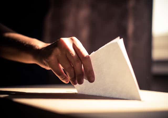 A hand placing a ballot in a ballot box
