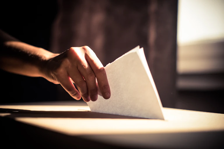 A hand placing a ballot in a ballot box